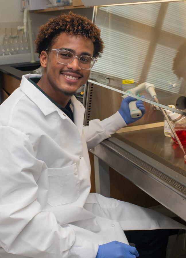 A student researcher smiles while holding lab equipment